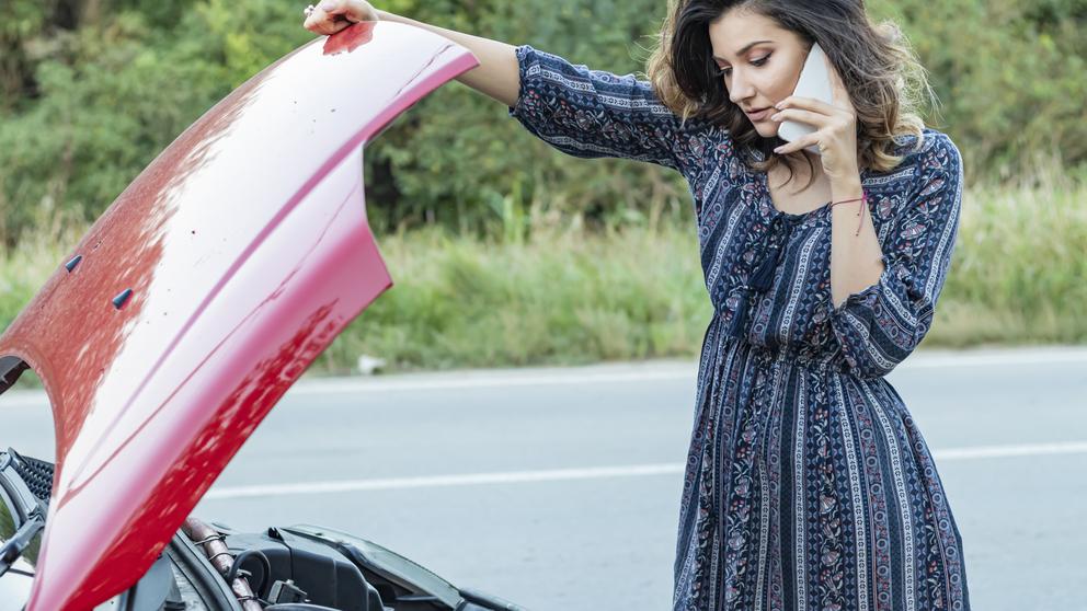 A woman inspecting her car after an accident on the road.