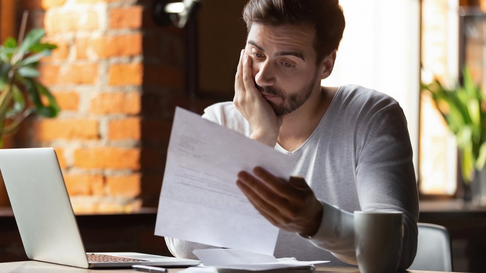 Confused frustrated man reading letter in cafe, receiving bad news